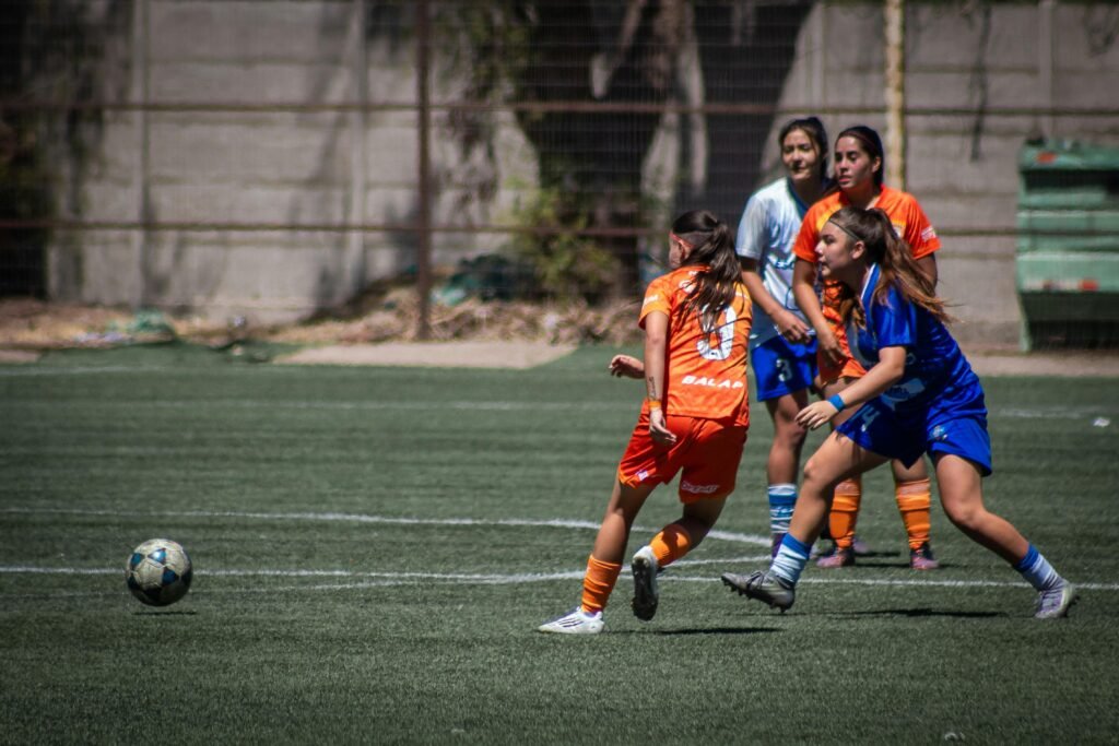Intense girls' soccer match with dynamic action on a sunny outdoor field.