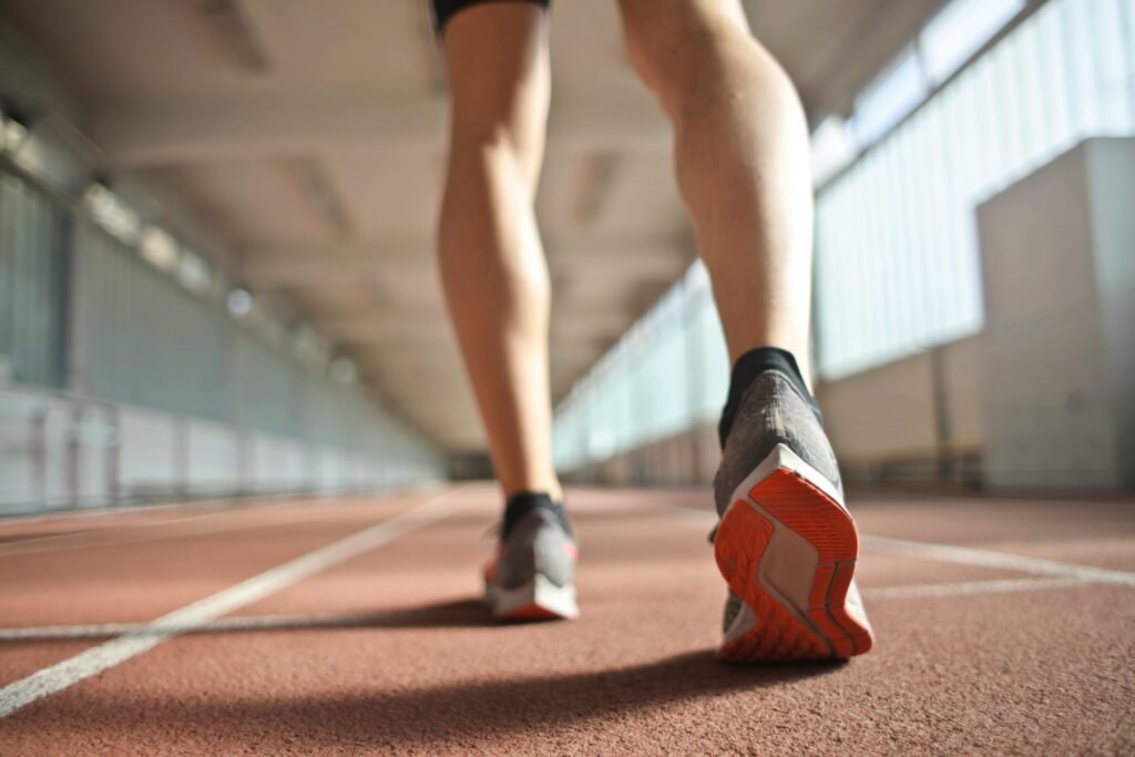 Back view of a runner's legs in a stadium, focusing on footwear and athletic motion.